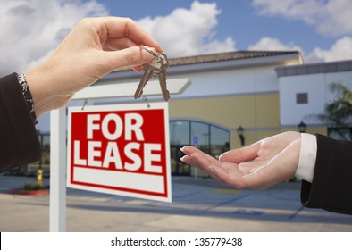 Real Estate Agent Handing Over the Keys in Front of Vacant Business Office and For Lease Sign.