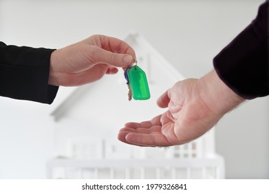 Real Estate Agent Handing Over Home Keys To A Home Buyer Against A White House. Mortgage, Housing Market, Home Loans, Rental And Property Management Concept.  No People. Copy Space