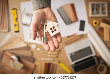 Real estate agent handing over a house key, desktop with tools, wood swatches and computer on background, top view - Shutterstock ID 267766277