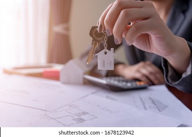 Real estate agent holding house key on table with house designs document,calculator,model house.Concept for real estate