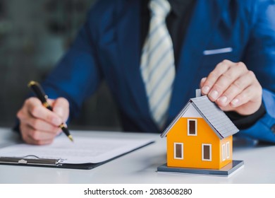 Real Estate Agent Home Sales Broker Is Using A Pen Pointing To The House Model And Explains The Business Contract, Rent, Buy, Mortgage, Loan, Or Home Insurance