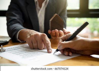 Real estate agent with house model hand putting signing contract,have a contract in place to protect it,signing of modest agreements form in office.Concept real estate,moving home or renting property