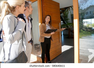 Real estate agent inviting couple to enter house for visit                     