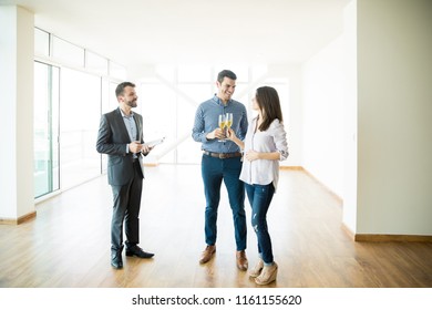 Real estate agent looking at couple celebrating with champagne toast in new apartment