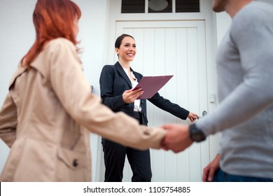 Real Estate Agent Near Door Inviting Young Couple To Enter House For Visit