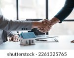 Real estate agent shakes hands with a client to sign a home purchase contract congratulating the client on the purchase.