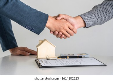 Real estate agent are shaking hands after good deal and giving house, keys to customer after signing contract to buy house with approved property application form.