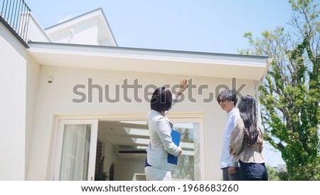 Real estate agent showing house exterior for asian couple.