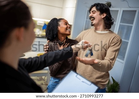 Real estate agent smiling while handing apartment keys to a mixed couple, symbolizing a successful move and new beginning.