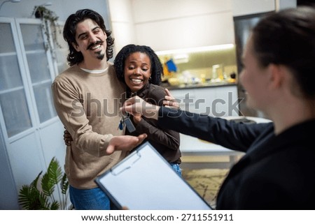 Real estate agent smiling while handing apartment keys to a mixed couple, symbolizing a successful move and new beginning.