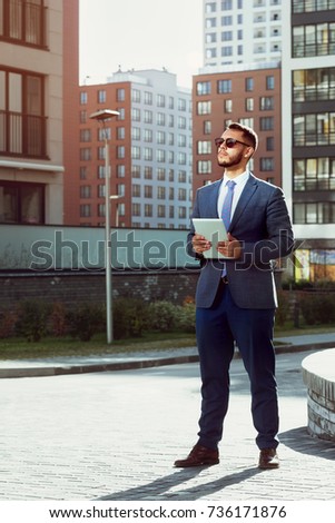 Real estate agent with tablet computer stands on modern city backdrop. Businessman or business concept