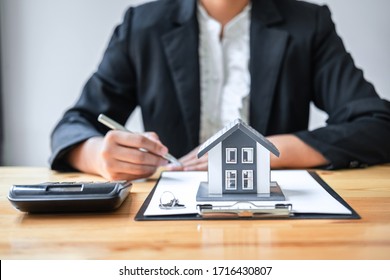 Real estate agent working sign agreement document contract for house insurance approving purchases for client with house model and key on table.