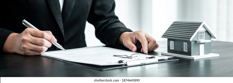 Real Estate Agent Working Sign Agreement Document Contract For Home Loan Insurance Approving Purchases For Client With House Model And Key On Table.