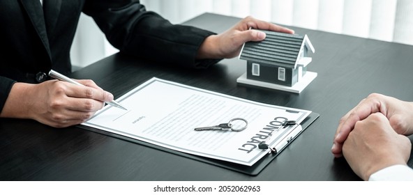 Real Estate Agent Working Sign Agreement Document Contract For Home Loan Insurance Approving Purchases For Client With House Model And Key On Table.