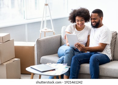 Real Estate Application. Cheerful African Spouses Using Tablet Computer Searching Apartment For Rent Online Sitting Together On Sofa At Home. House Hunting And Relocation Concept