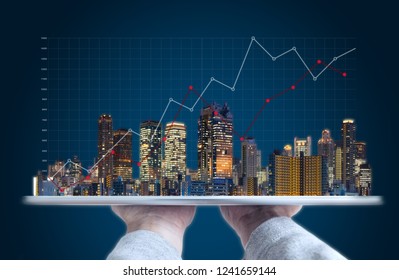 Real estate business investment and building technology. Hand holding digital tablet with buildings hologram and raising graph