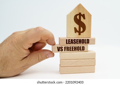 Real Estate And Business. On Wooden Blocks With The Inscription - Leasehold Vs Freehold, There Is A Model Of A House With A Dollar Symbol. The Man's Hand Takes Out The Block.