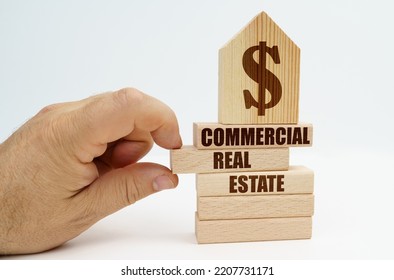 Real Estate And Business. On Wooden Blocks With The Inscription - Commercial Real Estate, There Is A Model Of A House With A Dollar Symbol. The Man's Hand Takes Out The Block.