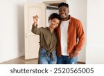 Real Estate. Cheerful African American Spouses Showing New House Key Smiling To Camera, Embracing Standing Among Moving Cardboard Boxes At Home. Relocation, Apartment Ownership And Family Housing