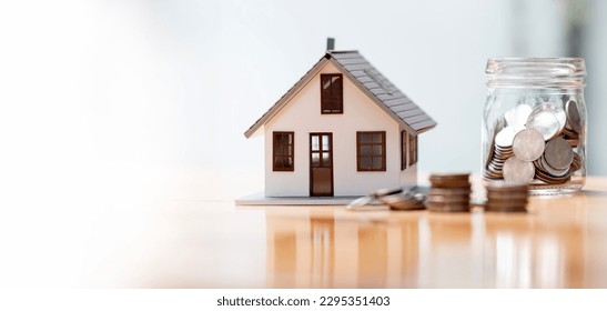 Real estate concept background. House model and coins stack on wooden table, copy space.