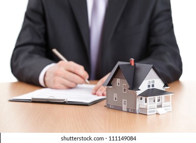 Real estate concept - businessman signs contract behind home architectural model