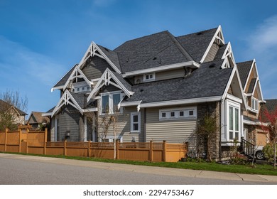 Real Estate Exterior Front House on a sunny day. Big custom made luxury house with front yard in spring. Roof shingles on top of the house. Dark asphalt tiles on the roof, black shingles, roof tile