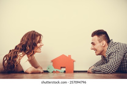 real estate, family and couple concept - smiling couple lying on floor with symbol house and key daydreaming at home, vintage filter