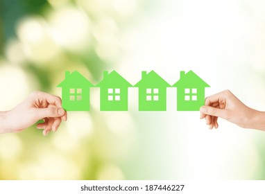 real estate and family home concept - closeup picture of male and female hands holding many green paper houses