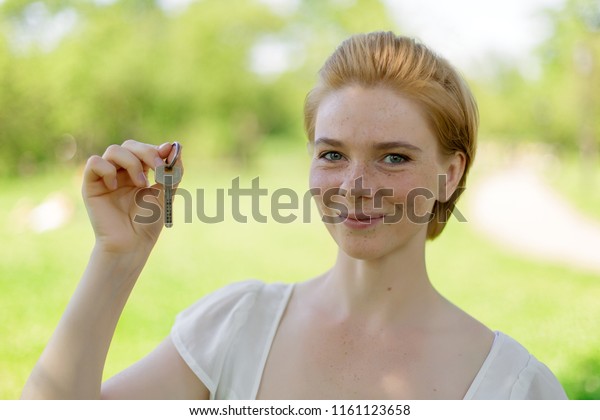 Real estate. Happy broker.\
Attractive young woman holding keys while standing outdoor against\
park