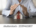 Real estate insurance agent making hand roof over small model of family house, promoting property buying, safety, offering security service, protection, mortgage consultation