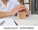 Real estate insurance. Man with wooden house figure at light table, closeup