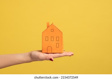 Real Estate Insurance, Repairing Services. Closeup Of Woman Hand Holding Small Orange Paper House, Concept Of Dream Home Purchase, Mortgage. Indoor Studio Shot Isolated On Yellow Background.