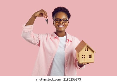 Real Estate, Moving Home Or Renting Apartment. Portrait Of Joyful Young African American Woman With Key And Small Wooden House In Her Hands. Happy Female Property Owner Isolated On Pink Background.