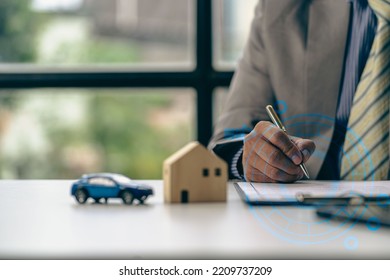 Real Estate Office, Sales Representatives Sitting At A Desk With Contract Documents And A Laptop And A Small House Next To It.