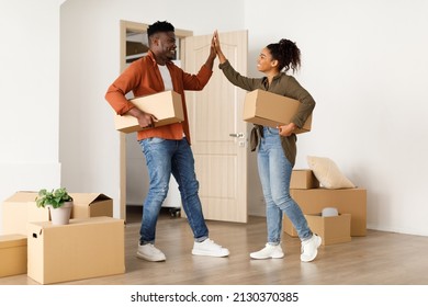 Real Estate Ownership. African American Couple Moving New House Holding Cardboard Boxes And Giving High Five Celebrating Relocation Entering Own Home, Standing Near Opened Door. Family Housing
