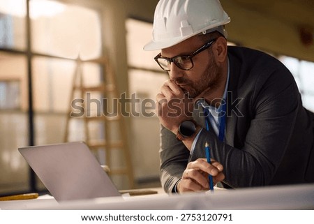 Real estate project manager using laptop while working on blueprints at construction site. 