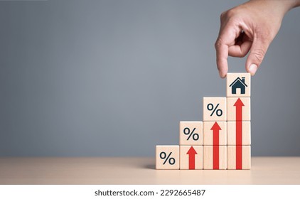 Real estate property investment concept. Asset management, Interest rates, inflation, loan mortgage, increase tax. Hand holding house icon on wooden cube from stack block with percent and rise arrow.