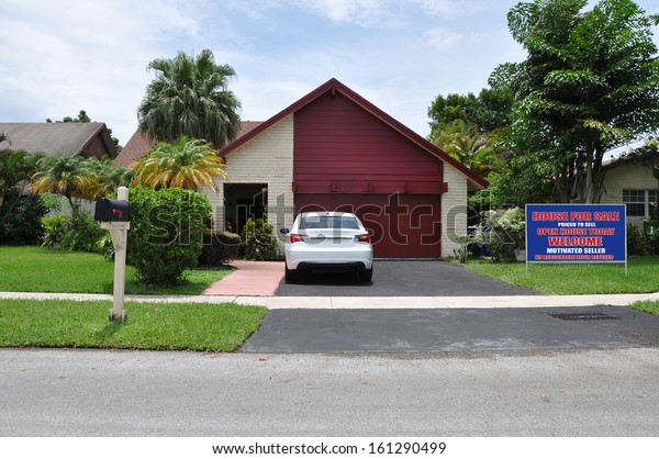 Real Estate For Sale Open House Welcome Sign on\
front yard lawn of Suburban Back Split Snout Garage style Home\
Parked Car Blue Sky Clouds