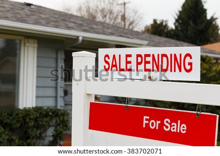 Real estate sign says for sale and pending on the top of it in front of a grey house.