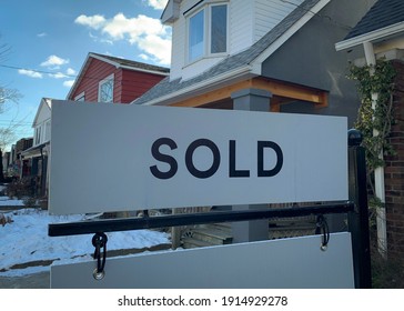 A Real Estate “sold” Sign Is Seen In Front Of Homes In The Winter Snow.