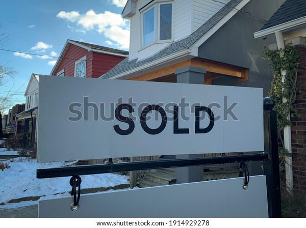 A real estate “sold” sign is seen in front of homes in the winter snow.