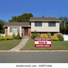 Real estate sold (another success let us help you buy sell your next home) sign Beautiful Suburban High Ranch Aluminum Siding Brownstone Brick Home residential neighborhood clear blue sky USA