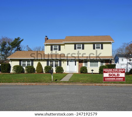 Real estate sold (another success let us help you buy sell your next home) sign Yellow McMansion style home clear blue sky autumn day residential neighborhood USA