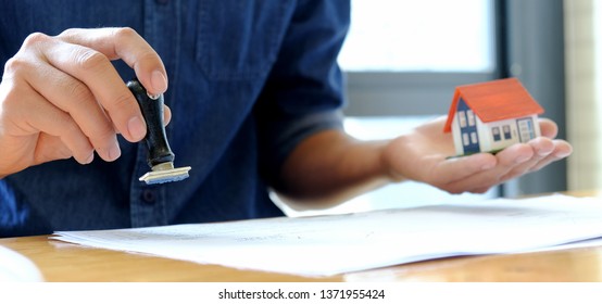Real Estate Trading Concept, Staff Holding A Rubber Stamp On Hand To Approve Sales.Model House On Hand And House Plan On The Table.