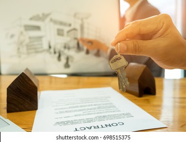 Real Estate Trading Concepts,Close-up House Key In Hand The Back Is A House Sketch,Model House And Contract Documents Placed On The Table.