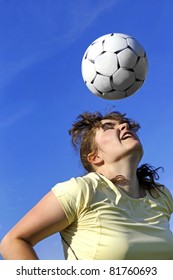 Real Female Soccer Or Football Player During A Match, Reaching To Hit The Ball With Her Head And Score A Goal With Sky And Stadium Spot Lights In Background.