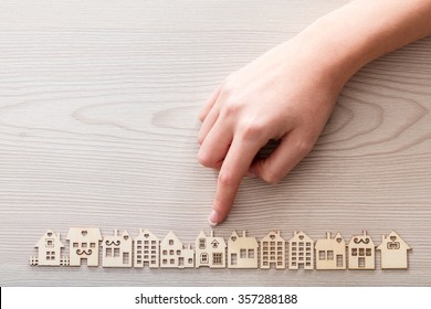 Real Hand Pointing Out A House Model Among The Others Mini Figures In A Micro Wooden Village Set