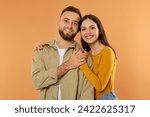 Real Love. Happy Young Family Couple Hugging And Holding Hands Symbolizing Their Romantic Bond, Smiling To Camera While Posing Over Orange Studio Background, Portrait Shot