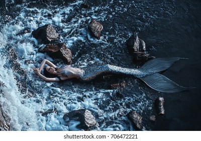 real mermaid posing relax resting ocean shore. Silver tail seductive body covered scales fashion model. Stylish idea summer photo shoot. fabulous mistress queen of  sea storm. chic wet long black hair