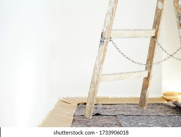 Real old wooden ladder of a painter in use for an interior renovation. Painter cover fleece for protection of floor surfaces. stepladder with chains and paint splashes. - Powered by Shutterstock